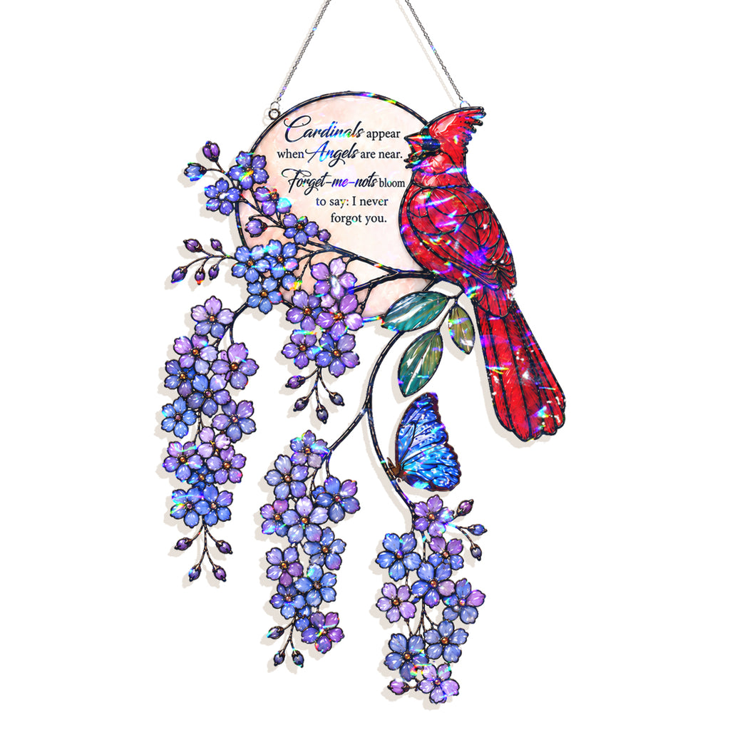 A decorative hanging ornament featuring a colorful cardinal bird perched on a flowering branch with purple blossoms and a blue butterfly. The ornament includes a circular inset with memorial-style text and is shown against a plain white background.