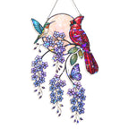 Stained glass hanging ornament featuring a red cardinal, a hummingbird, purple wisteria flowers, green leaves, and a purple butterfly against a pearlescent circular background, suspended by a silver string.
