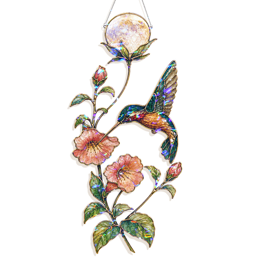 A hanging stained-glass style ornament featuring a hummingbird in iridescent blue, green, and gold tones, surrounded by pink flowers and green leaves, with a round moon panel at the top.
