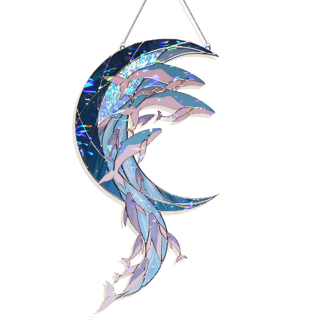 A hanging stained-glass style ornament shaped like a crescent moon with dolphins swimming through it. The design uses iridescent blue, lavender, and pale pink tones with metallic-looking reflective strips, suspended by thin metal wires against a plain white background.