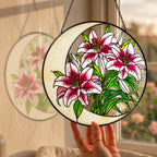 Pink lily stained glass suncatcher hanging in a sunny window with a garden view