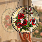 Red rose stained glass suncatcher held by a sunny window with a garden view