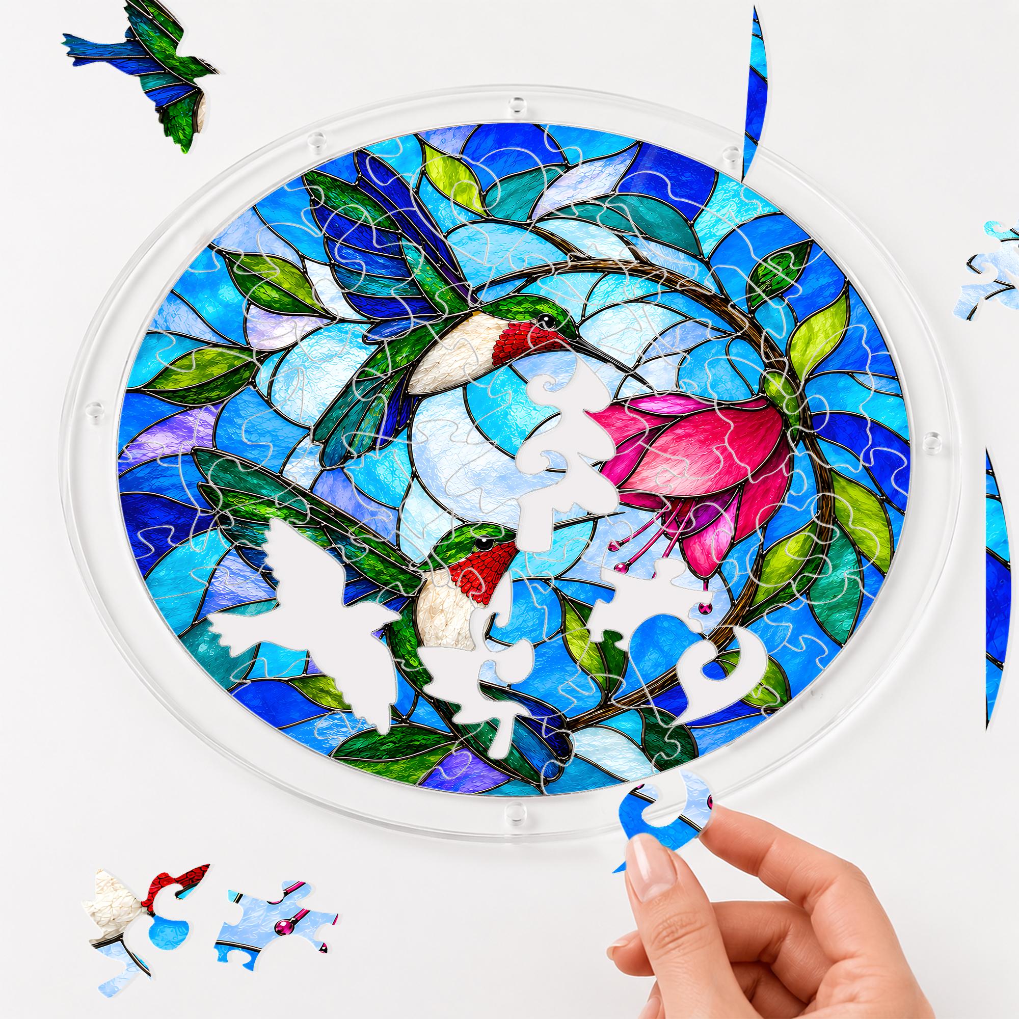 Hands assembling a round hummingbird and pink flower acrylic jigsaw puzzle suncatcher with interlocking pieces