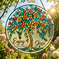 Decorative stained glass panel with floral design and text 'Enjoy Every Moment Jessi' against a natural background.
