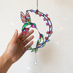 Hand holding a hummingbird cherry blossom moon holographic acrylic suncatcher against a light wall
