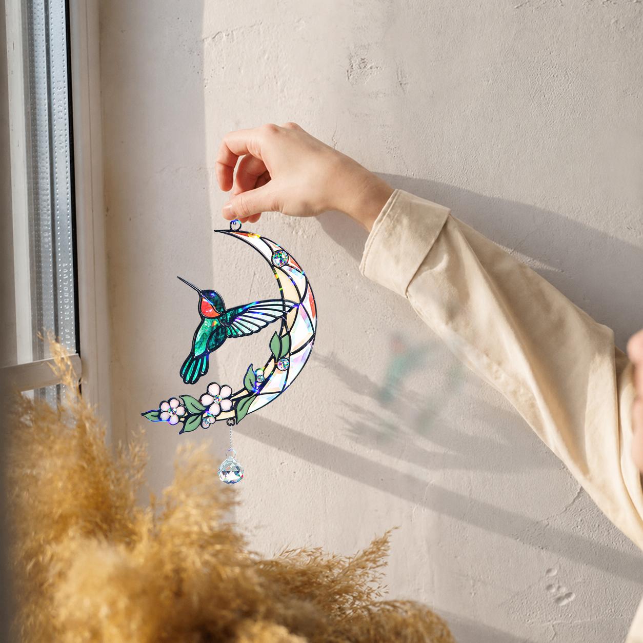 Hand hanging a hummingbird moon blossom holographic acrylic suncatcher near a bright window