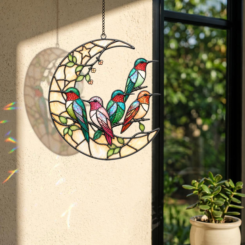 Hummingbird moon holographic acrylic suncatcher hanging on a bright window near soft pink flowers