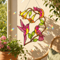 Colorful stained glass hummingbird and flower design hanging on a wall with plants and a chair in the background.