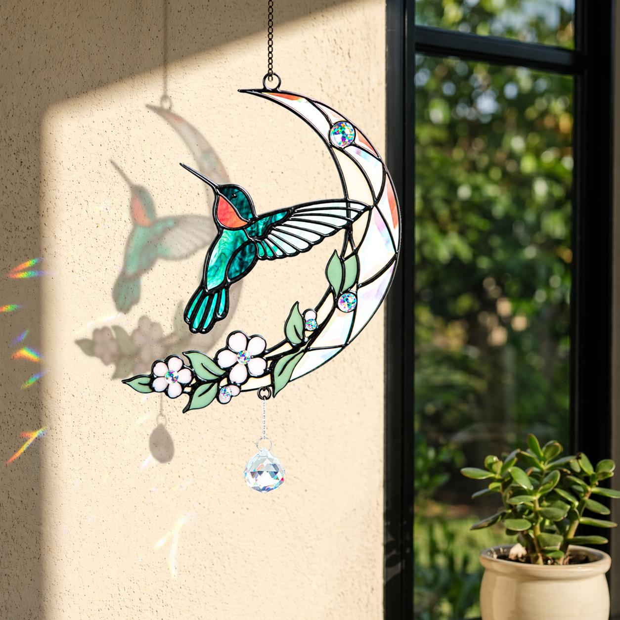Hummingbird moon blossom holographic acrylic suncatcher displayed by a bright window with soft natural light and greenery.