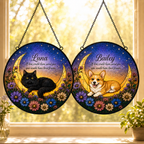 Personalized cat and dog moon memorial glass suncatchers hanging by a sunny window, featuring a black cat and corgi resting on crescent moons with flowers and starry sky artwork.