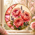 Round floral stained glass panel with pink peonies and green leaves, hanging in front of a window with pink flowers.