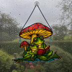 Frog couple reading suncatcher on a rain-streaked window with a green garden behind