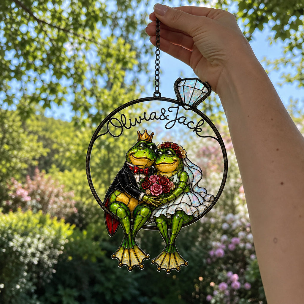 Hand holding the personalized frog wedding couple ring suncatcher by its chain outdoors