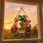 Frog couple scooter suncatcher on a rainy window with a garden path behind