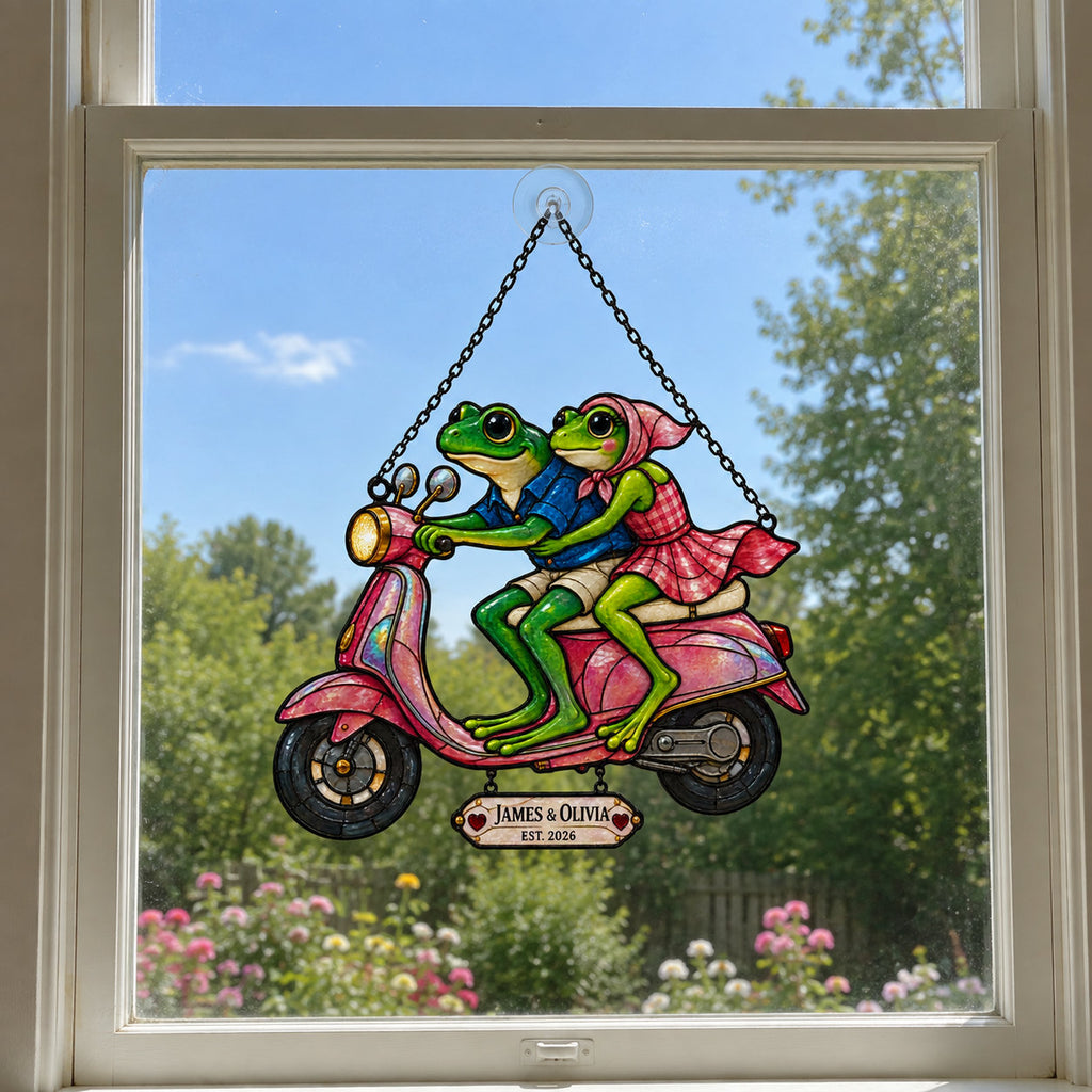 Personalized frog couple scooter suncatcher hanging in a bright window under a blue sky