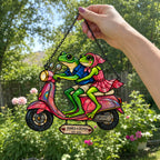 Hand holding the personalized frog couple scooter suncatcher by its chain outdoors