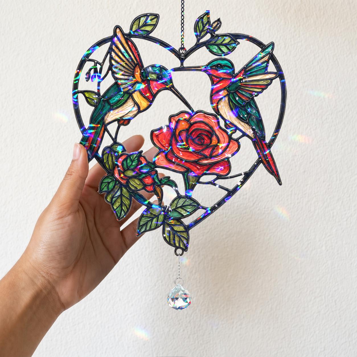 Hand holding the heart-shaped hummingbird rose suncatcher to show its colorful holographic broken glass finish.