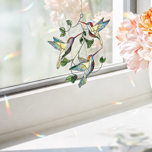 Hummingbird Leaf acrylic suncatcher hanging near a bright window with pink flowers and subtle rainbow light reflections.