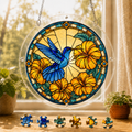 Round Azure Hibiscus Flight Hummingbird acrylic puzzle suncatcher hanging in a sunny window with colorful loose puzzle pieces below.