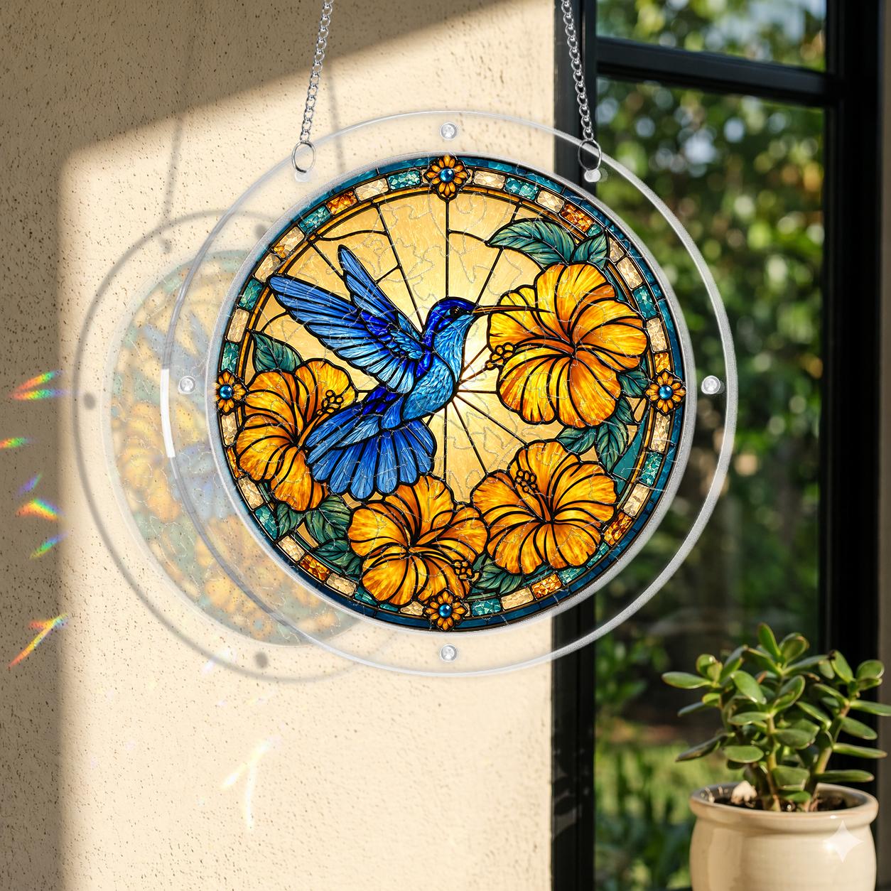 Round acrylic hummingbird puzzle suncatcher hanging in a window with orange hibiscus flowers and golden artwork.