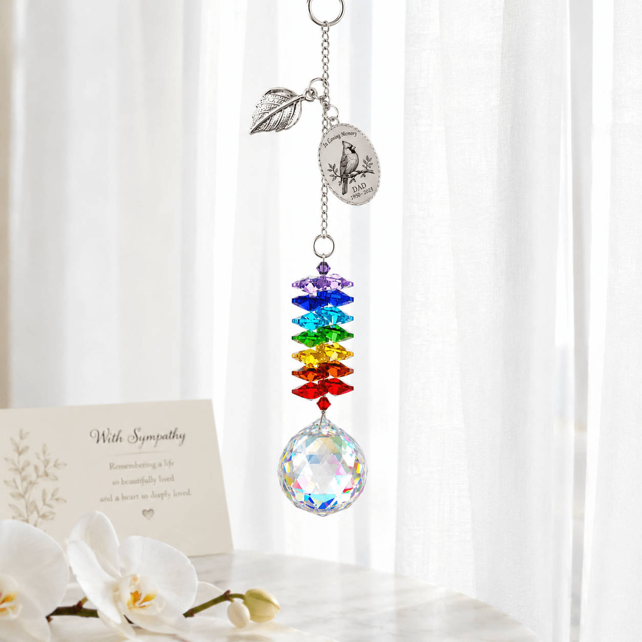 Personalized cardinal memorial crystal suncatcher hanging in front of sheer curtains with remembrance card and soft white flowers