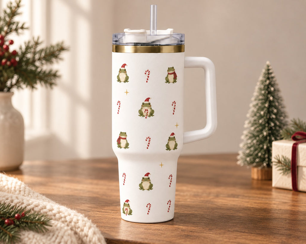 White Christmas frog 40 oz tumbler with handle and straw on a wooden table beside a mini Christmas tree