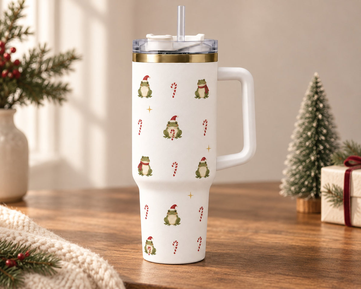 White Christmas frog 40 oz tumbler with handle and straw on a wooden table beside a mini Christmas tree