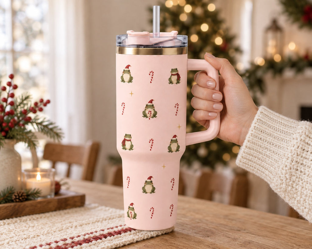 Hand holding the light pink Christmas frog tumbler by its handle in a cozy living room