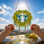 Yellow wisteria hummingbird acrylic puzzle suncatcher held against a blue sky and garden background.
