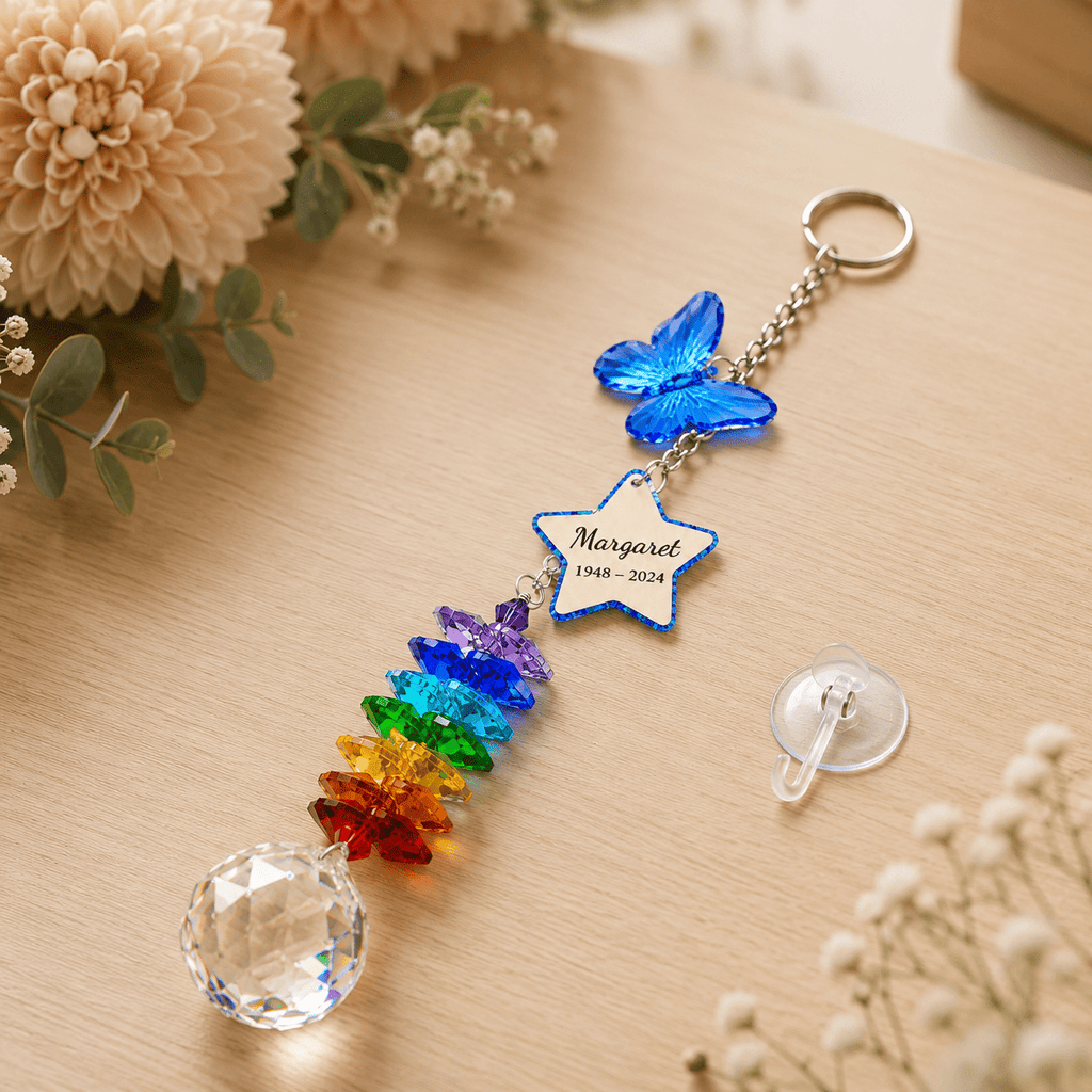 Personalized memorial butterfly crystal suncatcher displayed on wooden tabletop with blue butterfly charm, custom star charm, rainbow crystal strand, and clear crystal ball