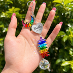 Hand holding personalized dog memorial Rainbow Bridge crystal suncatcher outdoors with green garden background and sunlight