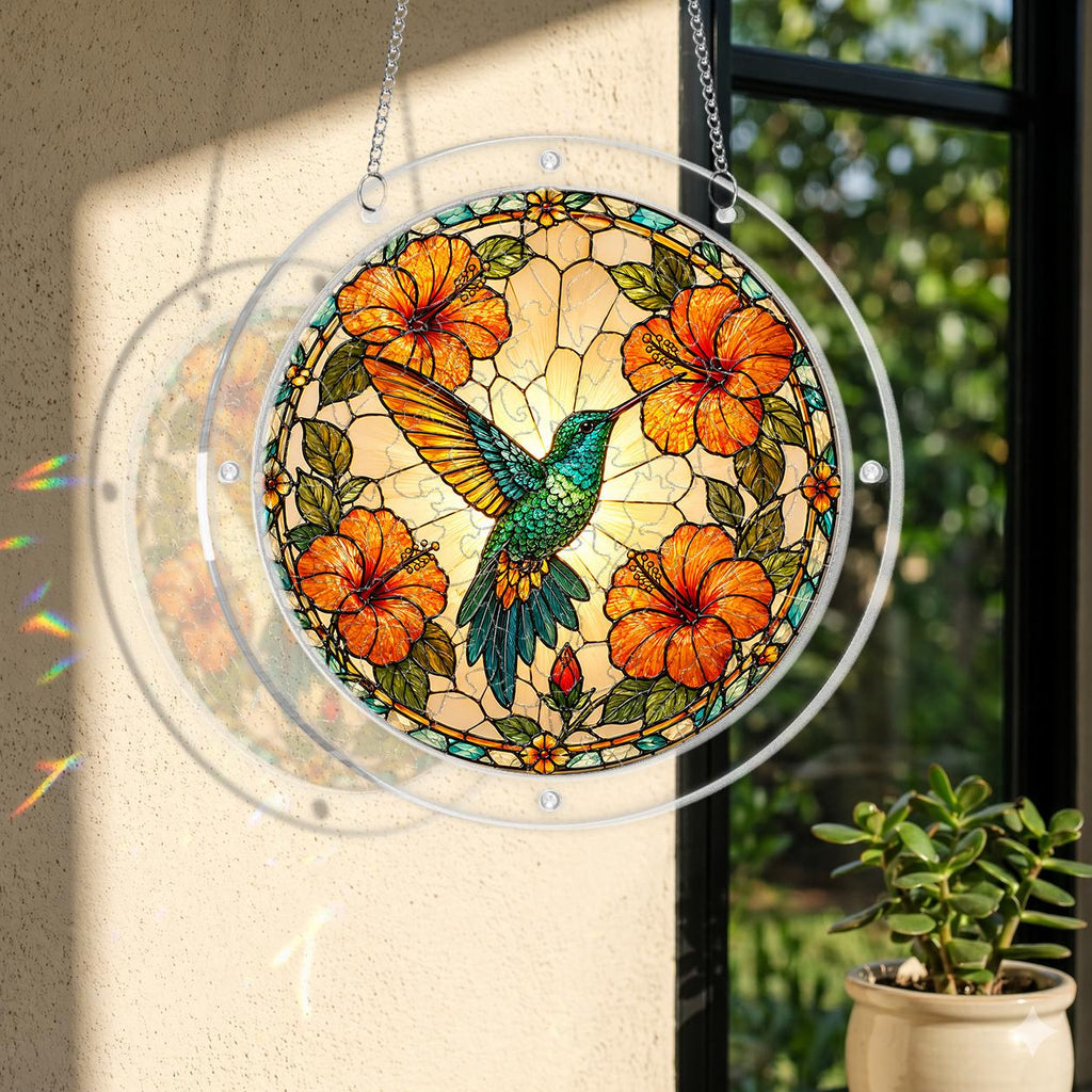 Round acrylic hummingbird puzzle suncatcher hanging by a window with orange hibiscus flowers and warm golden artwork.