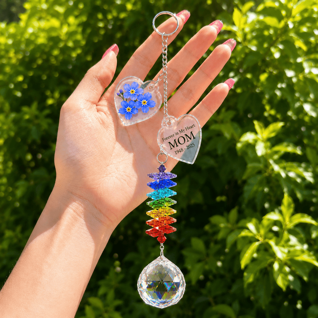 Hand holding personalized forget me not memorial crystal suncatcher outdoors with blue flower charm, custom star charm, rainbow crystal strand, and sparkling crystal ball