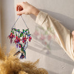 Close-up of a hand holding the Fuchsia Hummingbird holographic acrylic suncatcher, showing the colorful fuchsia flowers, hummingbird artwork, and rainbow broken-glass shimmer.