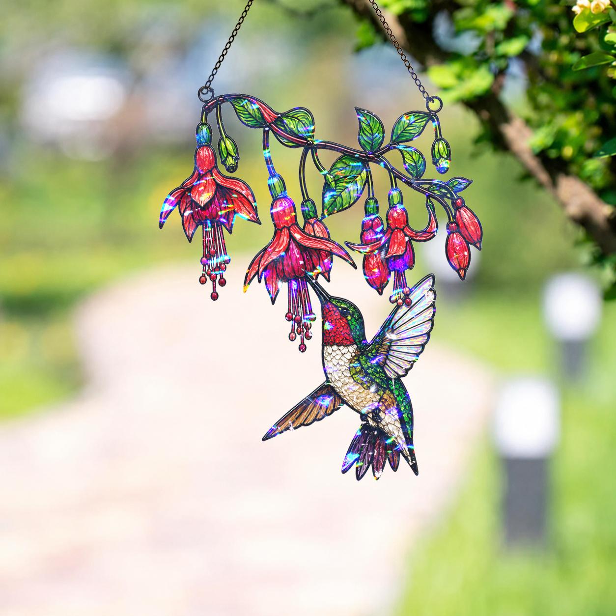 Fuchsia Hummingbird holographic acrylic suncatcher hanging outdoors in a sunny garden setting with green foliage and soft background blur.
