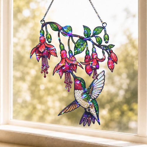 Fuchsia Hummingbird holographic acrylic suncatcher hanging in a sunny window, creating colorful rainbow reflections with a soft garden view in the background.