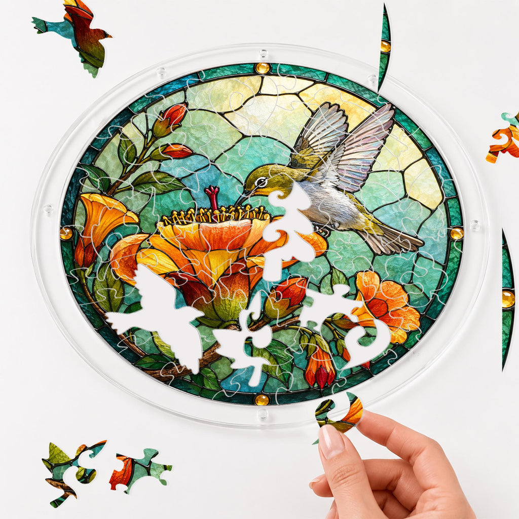 Hand assembling a hummingbird orange flower acrylic puzzle suncatcher with colorful puzzle pieces and clear acrylic frame