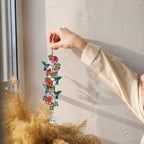 Hummingbird flower vine holographic acrylic suncatcher held near a sunny wall with warm natural light and soft shadows.
