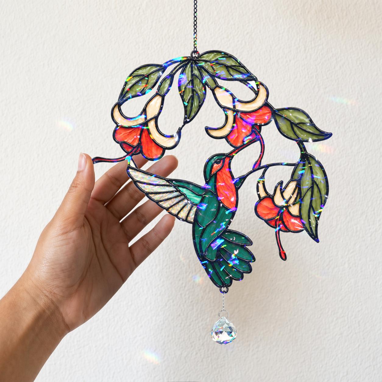 Hand holding hummingbird fuchsia flower holographic acrylic suncatcher against a white wall for size reference.
