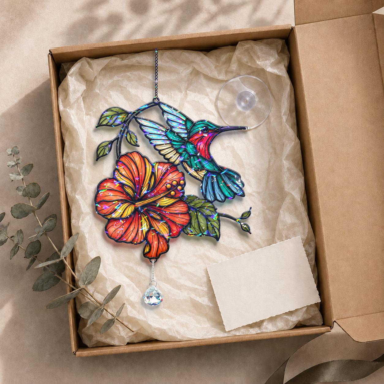 Hummingbird hibiscus holographic acrylic suncatcher displayed in a kraft gift box with tissue paper and adhesive hook.
