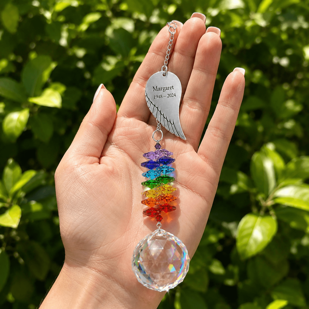 Hand holding personalized memorial angel wing crystal suncatcher outdoors with custom Margaret wing charm, rainbow crystals, and sparkling crystal ball