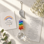 Personalized memorial angel wing crystal suncatcher displayed on marble surface with Rainbow Bridge remembrance card and soft sunlight