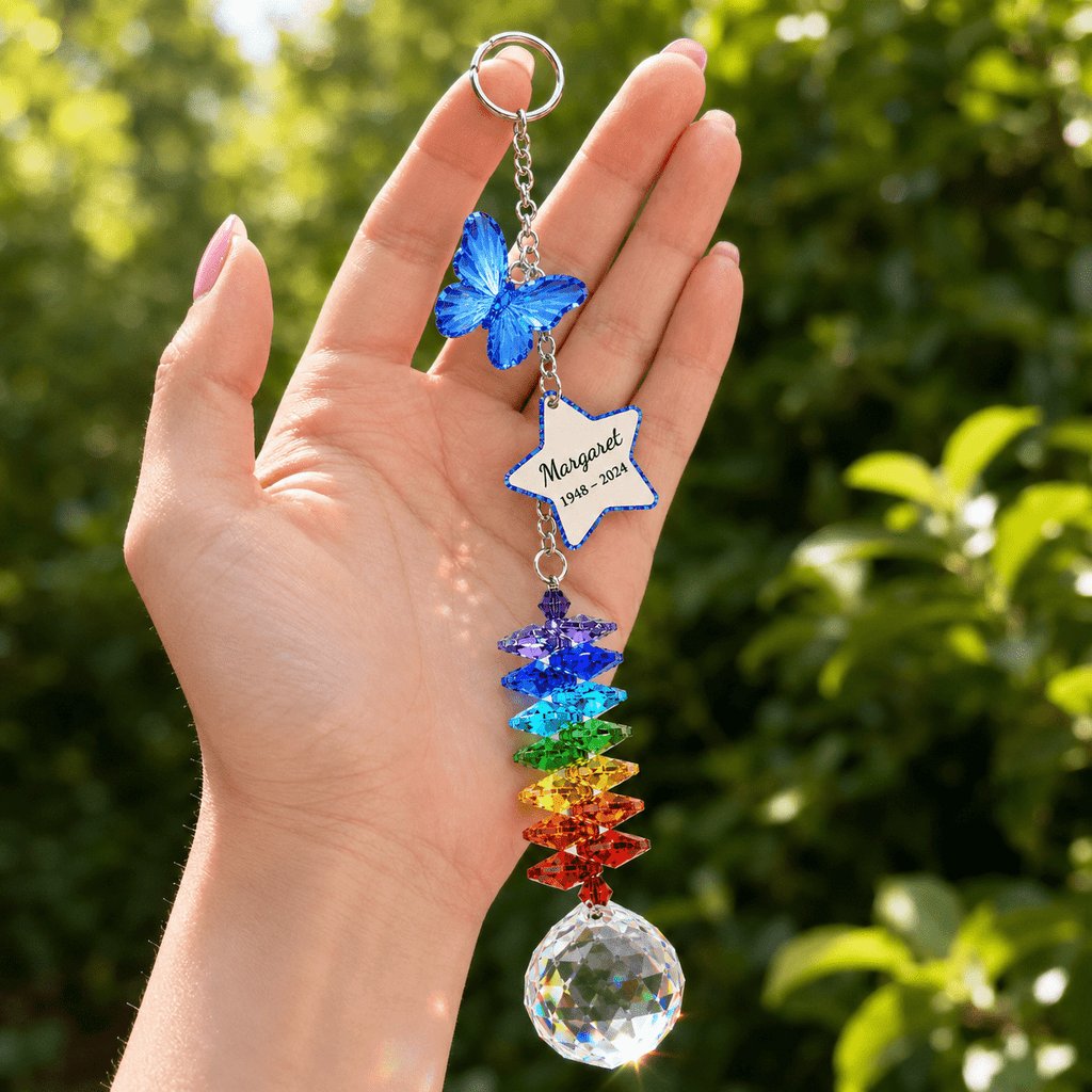Hand holding personalized memorial butterfly crystal suncatcher outdoors with blue butterfly charm, custom star charm, rainbow crystals, and sparkling crystal ball