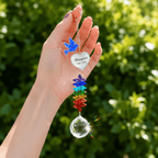 Hand holding personalized memorial dove crystal suncatcher outdoors with blue dove charm, custom heart charm, rainbow crystals, and sparkling crystal ball