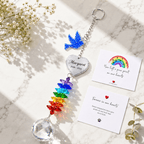 Personalized memorial dove crystal suncatcher displayed on marble surface with sympathy cards, rainbow crystals, and white flowers