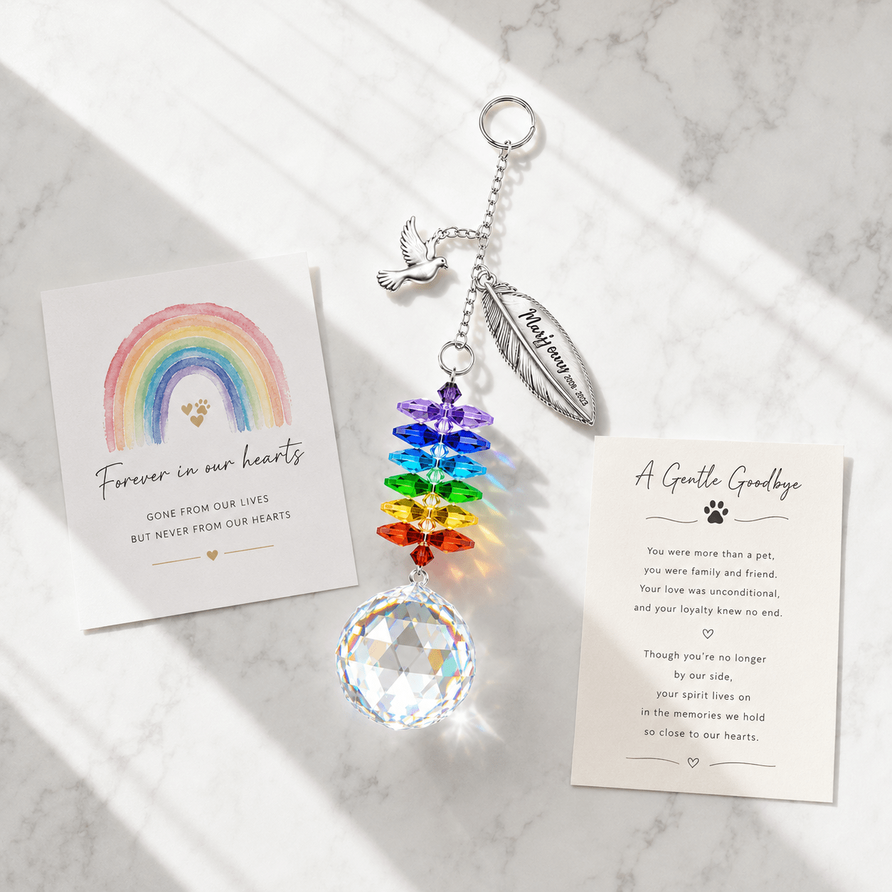 Personalized memorial feather dove crystal suncatcher displayed on marble surface with sympathy cards, rainbow crystals, and soft sunlight