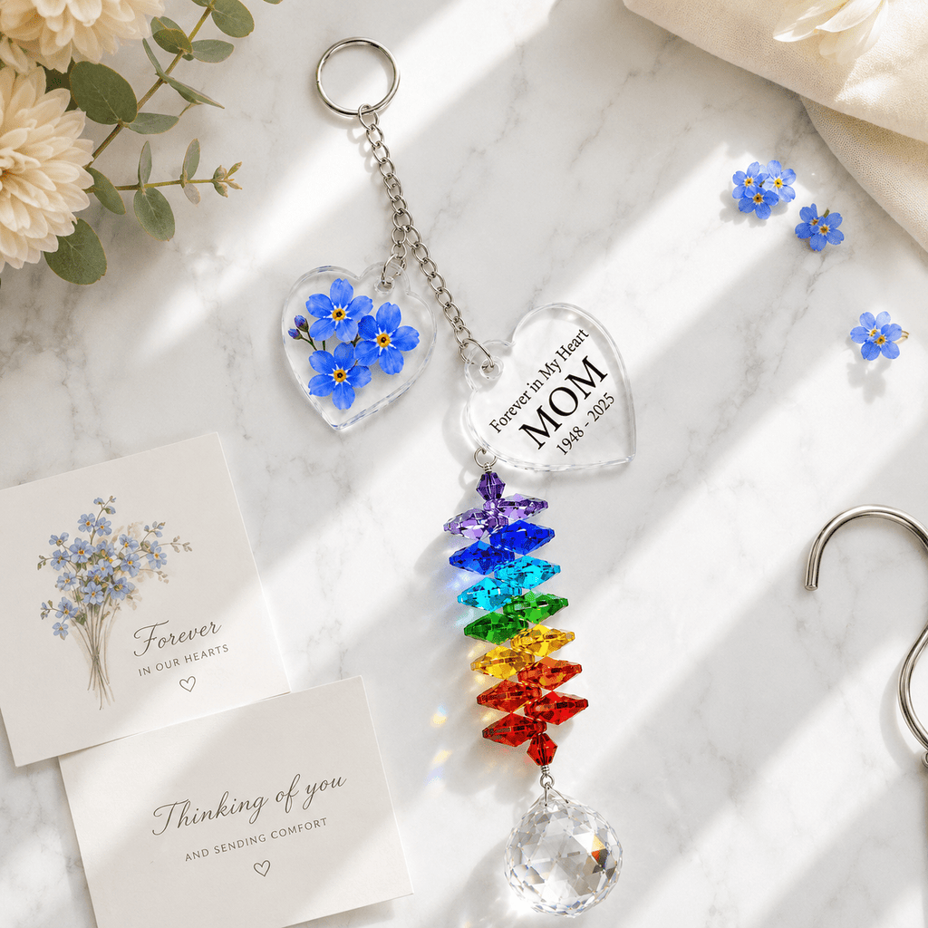 Personalized forget me not memorial crystal suncatcher displayed on marble surface with sympathy cards, blue flower charm, rainbow crystals, and soft sunlight
