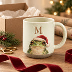 Initial frog pottery mug next to a kraft gift box, red velvet ribbon and wrapping paper