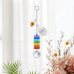 Personalized birth flower crystal suncatcher hanging in front of soft white curtains with marigold heart charm, custom Emma teardrop charm, rainbow crystals, and clear crystal ball