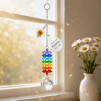 Personalized birth flower crystal suncatcher hanging by a sunny window beside a white vase of daisies with rainbow crystal reflections